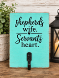 A turquoise wooden sign with black script text reading 'shepherds wife. Servants heart.