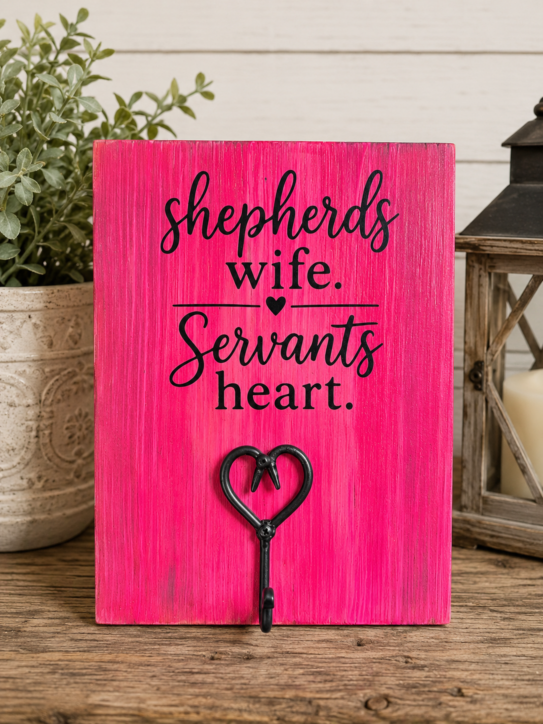 A rectangular pink wooden sign with black script text reading 'shepherds wife. Servants heart.